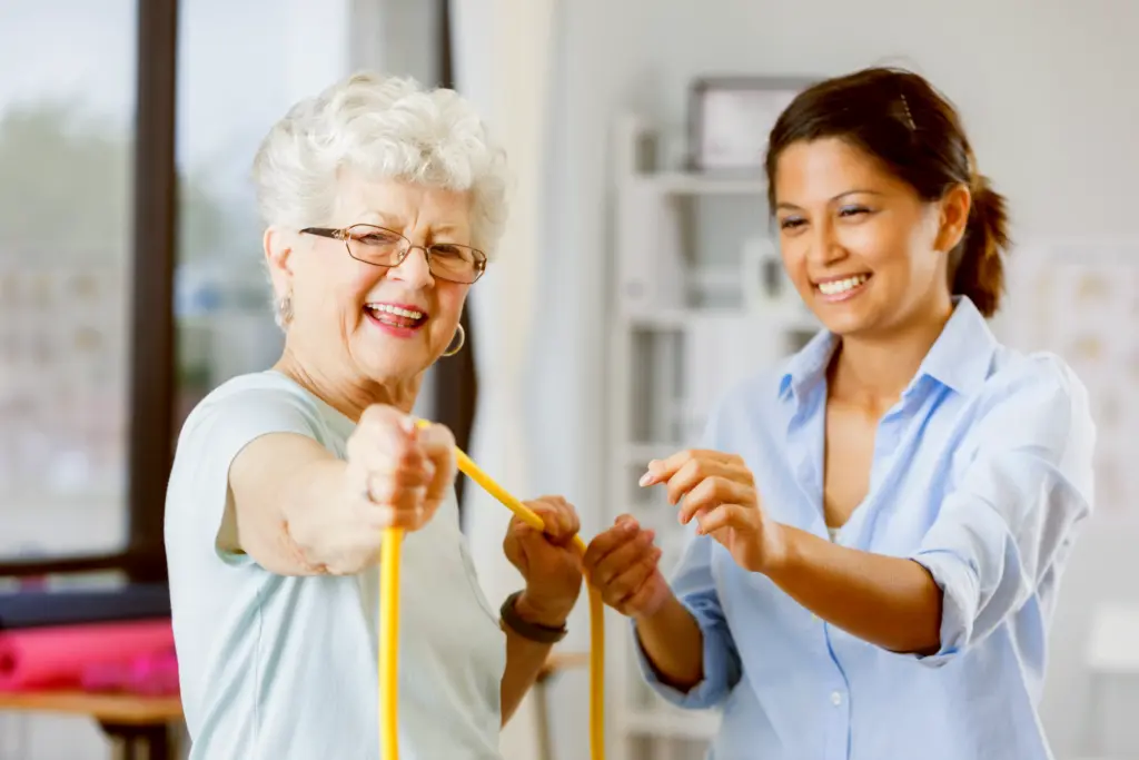 Eine Ergotherapeutin unterstützt eine fröhliche Seniorin beim Training