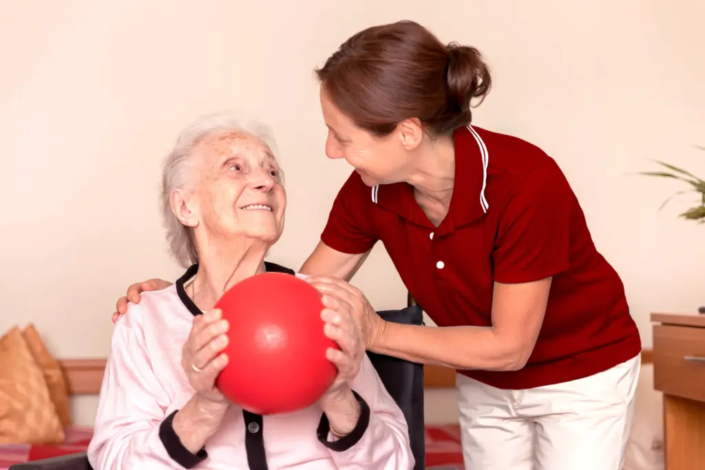 Eine Therapeutin und eine Seniorin sind in eine ergotherapeutische Übung mit einem Ball vertieft