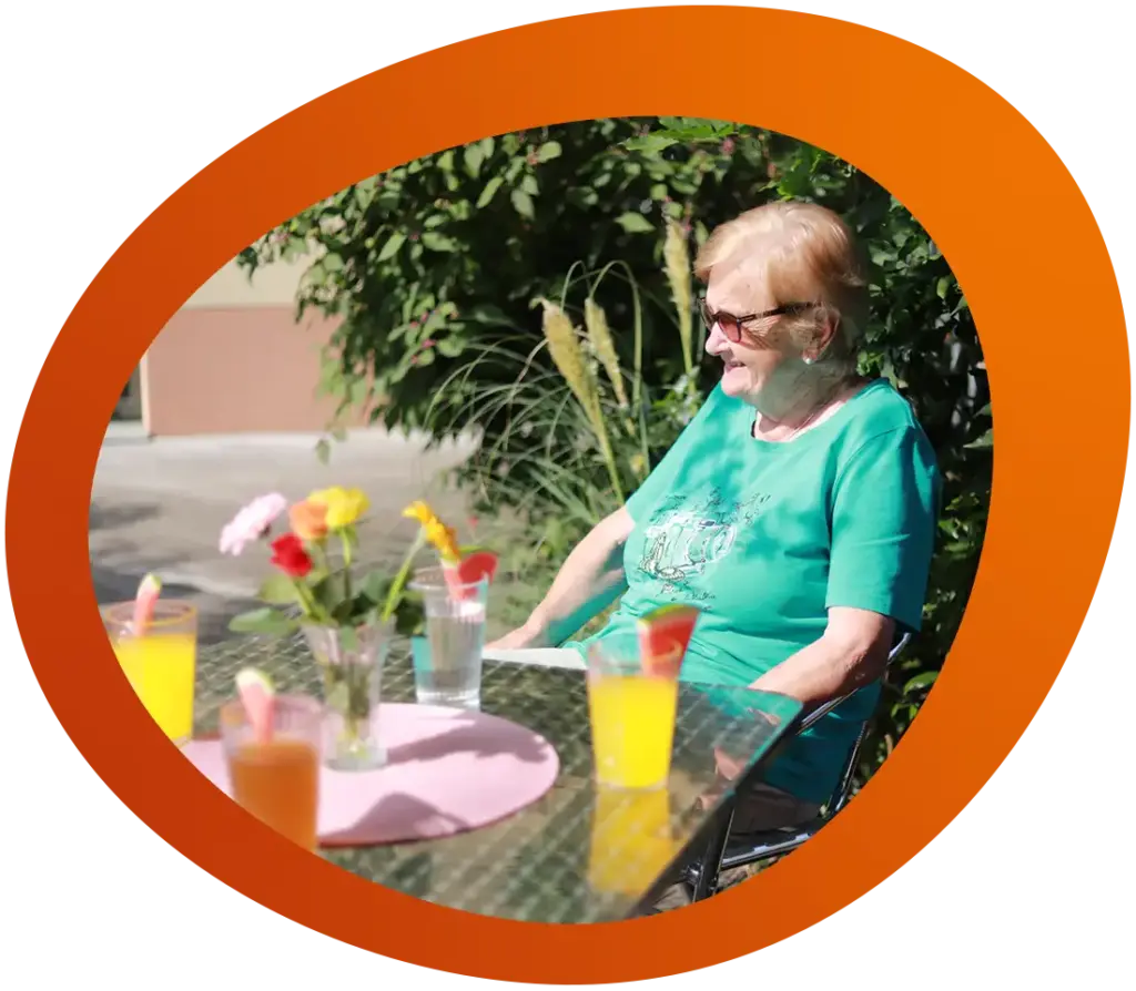 Eine Seniorin sitzt im strahlenden Sonnenschein auf der Terrasse und genießt einen Orangensaft
