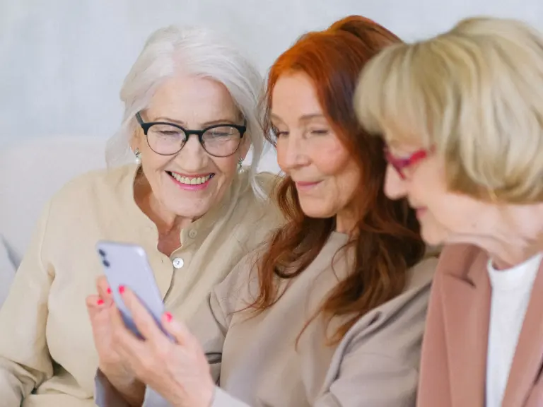 Drei Seniorinnen schauen sich ein Video auf einem Smartphone an und haben Spaß