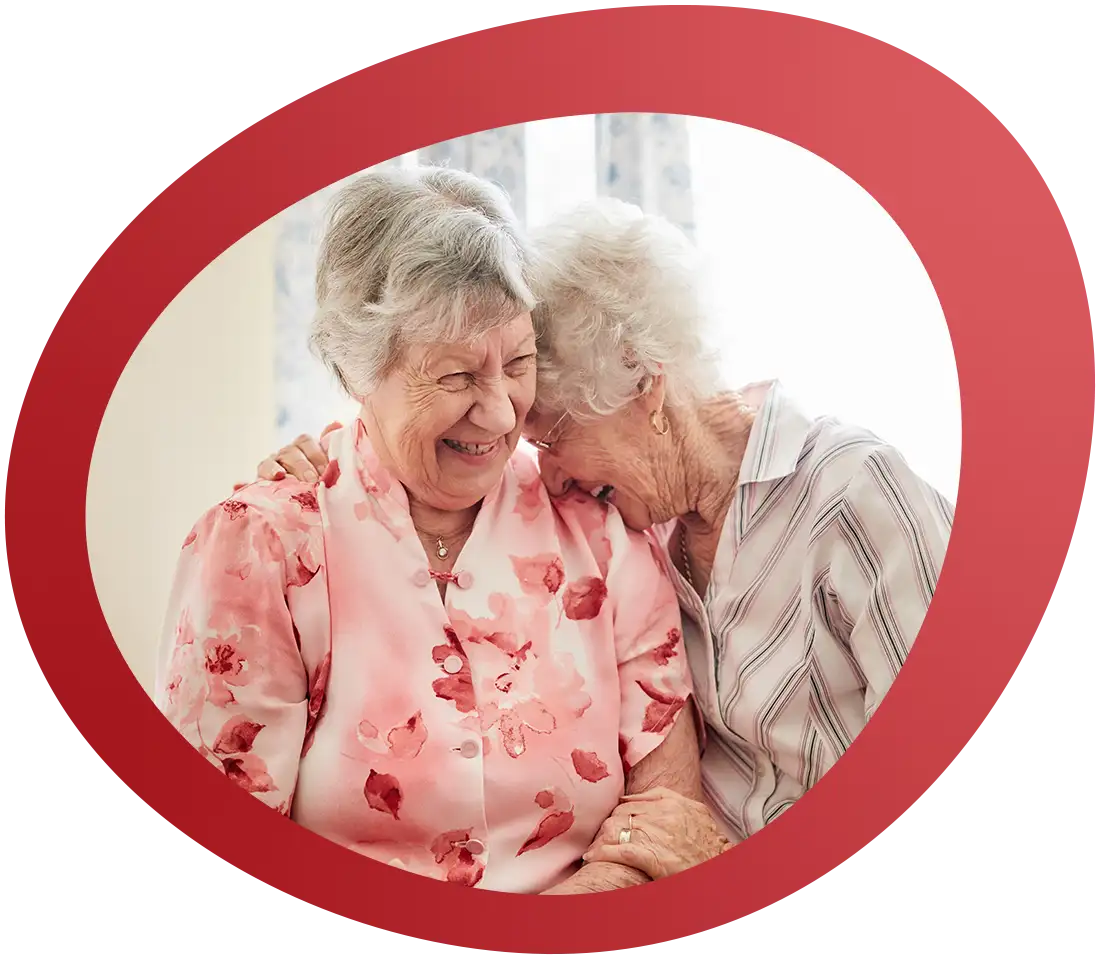 Zwei Seniorinnen lehnen sich vertraut aneinander und lachen gemeinsam