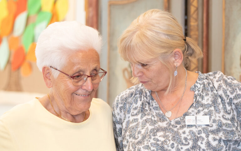 Ein Tagespflegegast und eine Pflegefachkraft unterhalten sich lächelnd