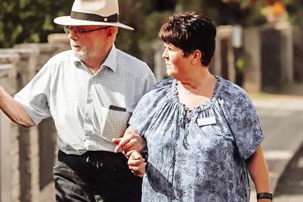 Alltagsbegleiterin geht mit einem Senior untergehakt spazieren
